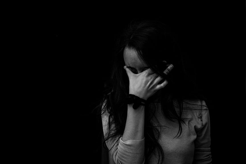 Černobílá fotografie unavené ženy, která si drží tvář v dlani. 