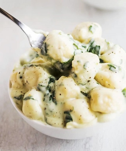 Gnocchi se špenátem a krémovou bílou omáčkou v bílé misce.