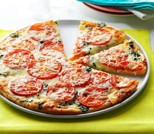 Špenátová pizza s mozzarellou a rajčaty na bílém talíři.