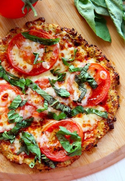 Dietní večeře ve formě zdravé pizzy s bylinkami a rajčaty, servírované na dřevěném podnosu.