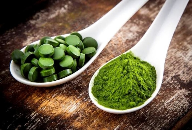 Chlorella tabletky a prášek ze zeleného ječmene na bílých lžičkách