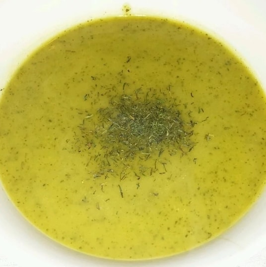 Krémová cuketová polévka s bylinkami v bílém hlubokém talíři