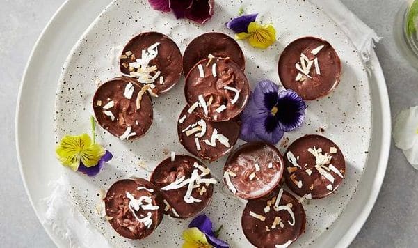 Zdravé velikonoční cukroví z čokolády a kokosu s okvětními lístky květin na flekatém keramickém talíři