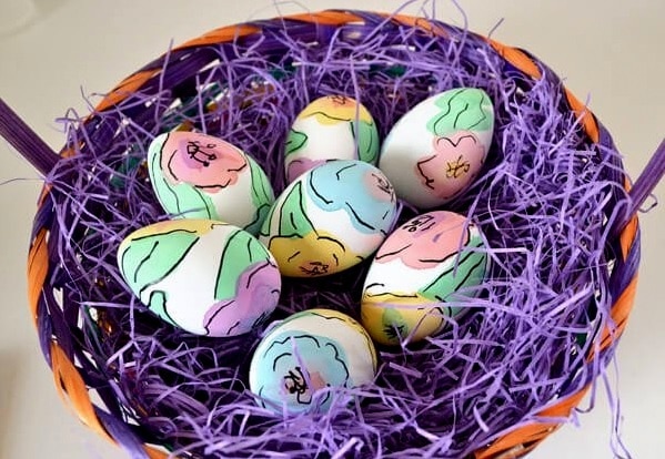 Zdobená velikonoční vejce v proutěném košíku s fialovou dekorací